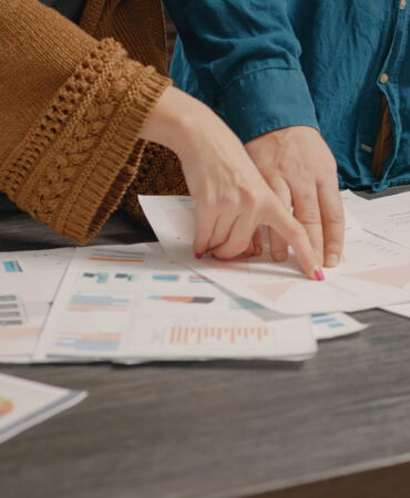 Close up of people checking papers with data rate charts on table. Workmates looking at files to plan business project and marketing strategy. Colleagues working on presentation.